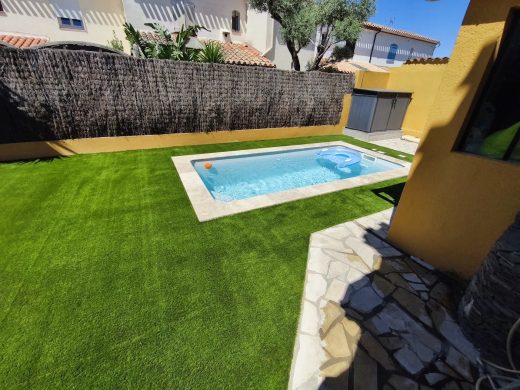 Gazon synthétique autour d’une piscine, jardin clos par un brise-vue en bruyère