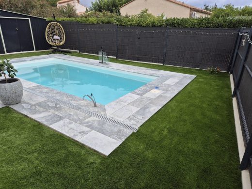 Piscine entourée de gazon synthétique et de panneaux occultants