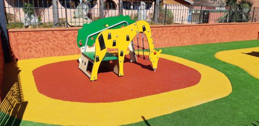 Jeu girafe sur un sol amortissant coulé rouge et jaune, entouré de gazon synthétique